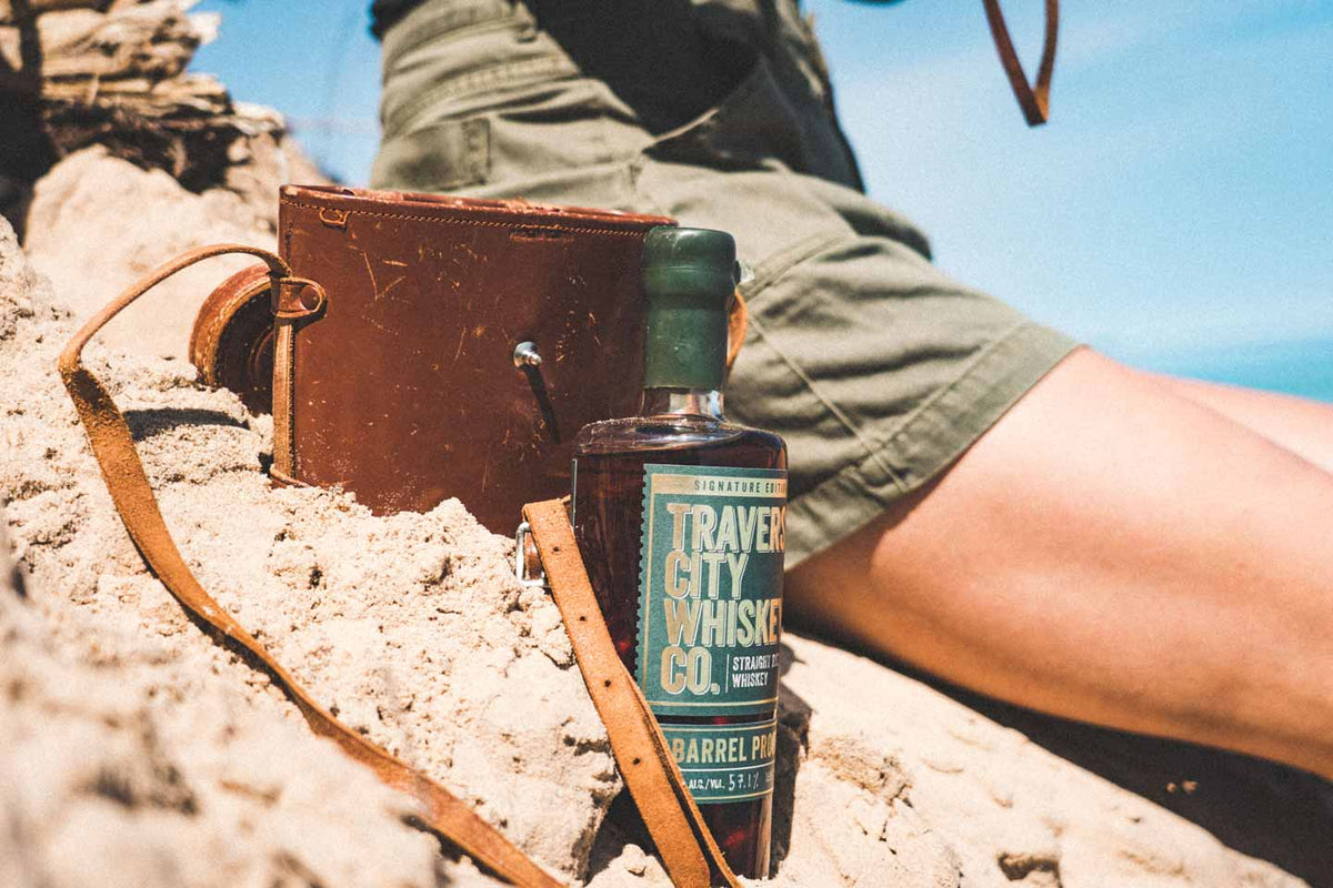 Barrel Proof Rye bottle on the sand next to a leather journal