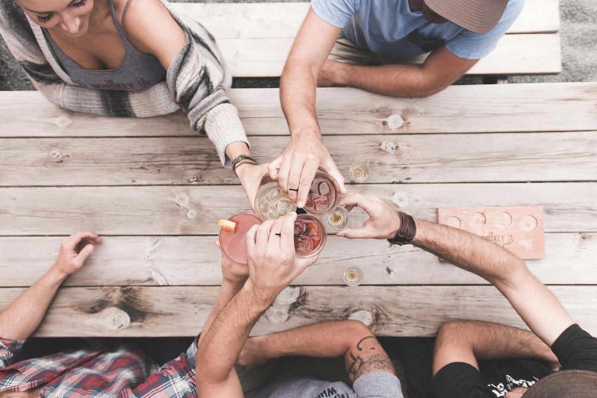 Friends toasting with whiskey glasses at a wooden table
