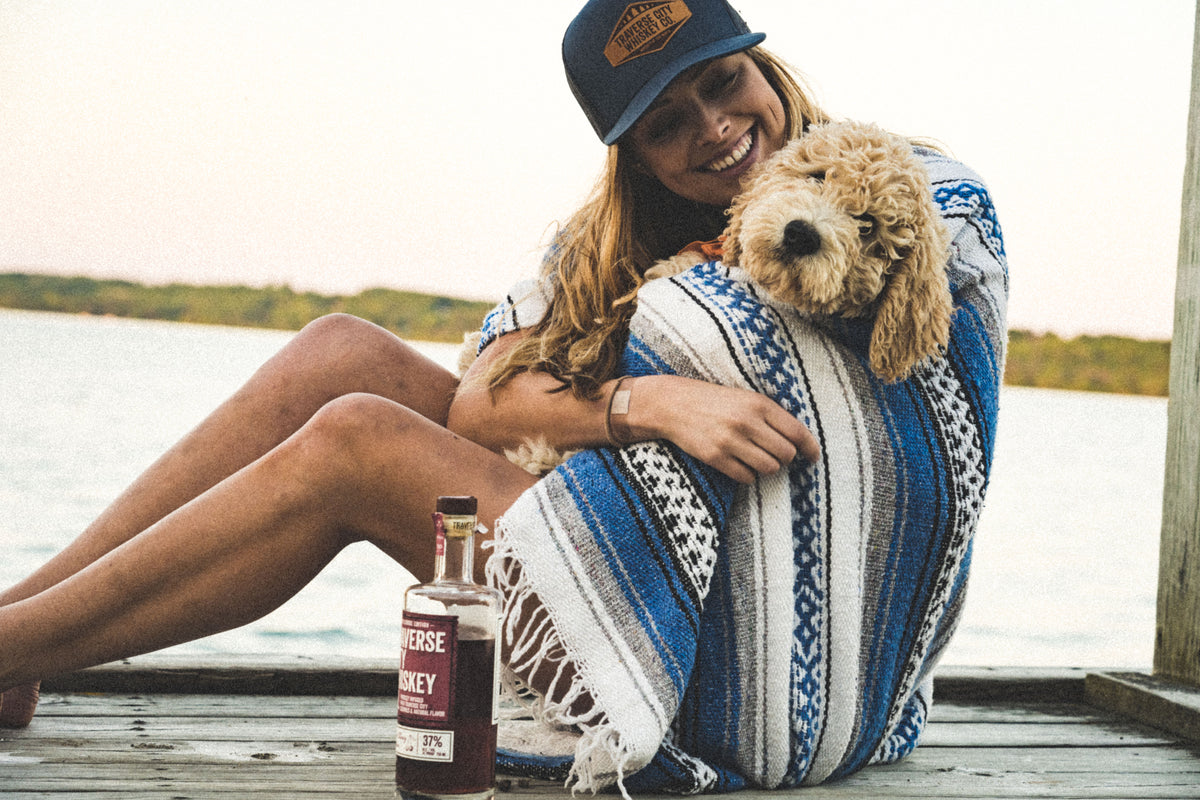 Woman with her dog on a lakeside dock next to a bottle of American Cherry Edition