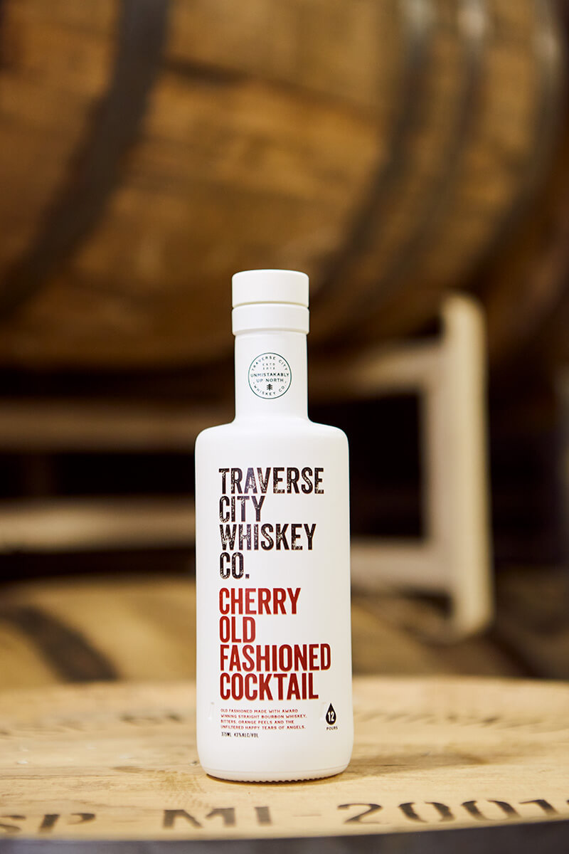 Ready-to-Serve Cherry Old Fashioned bottle on a whiskey barrel