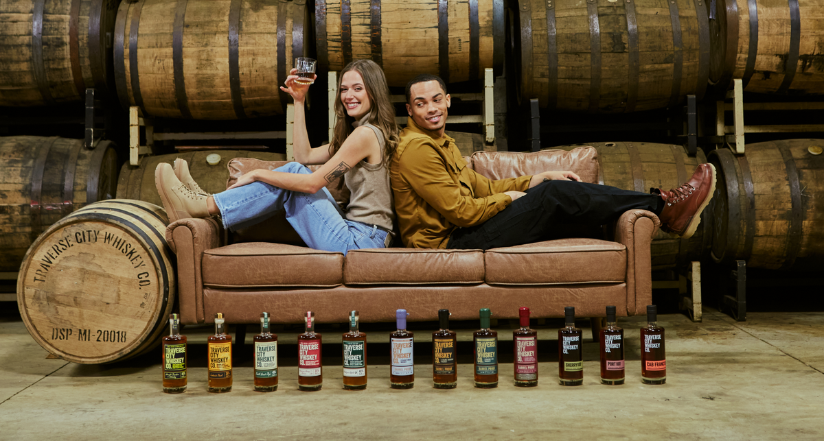 Couple relaxing on a leather couch in the rickhouse with a lineup of whiskey bottles