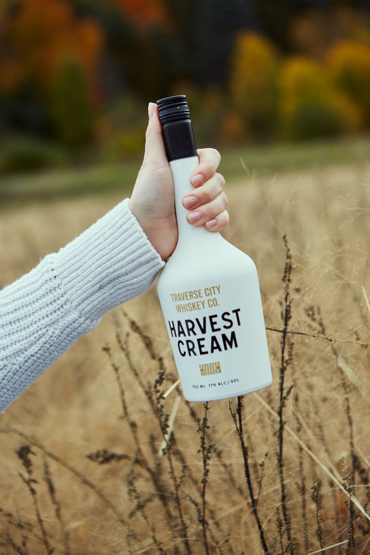 Hand holding a bottle of Harvest Cream in a golden field