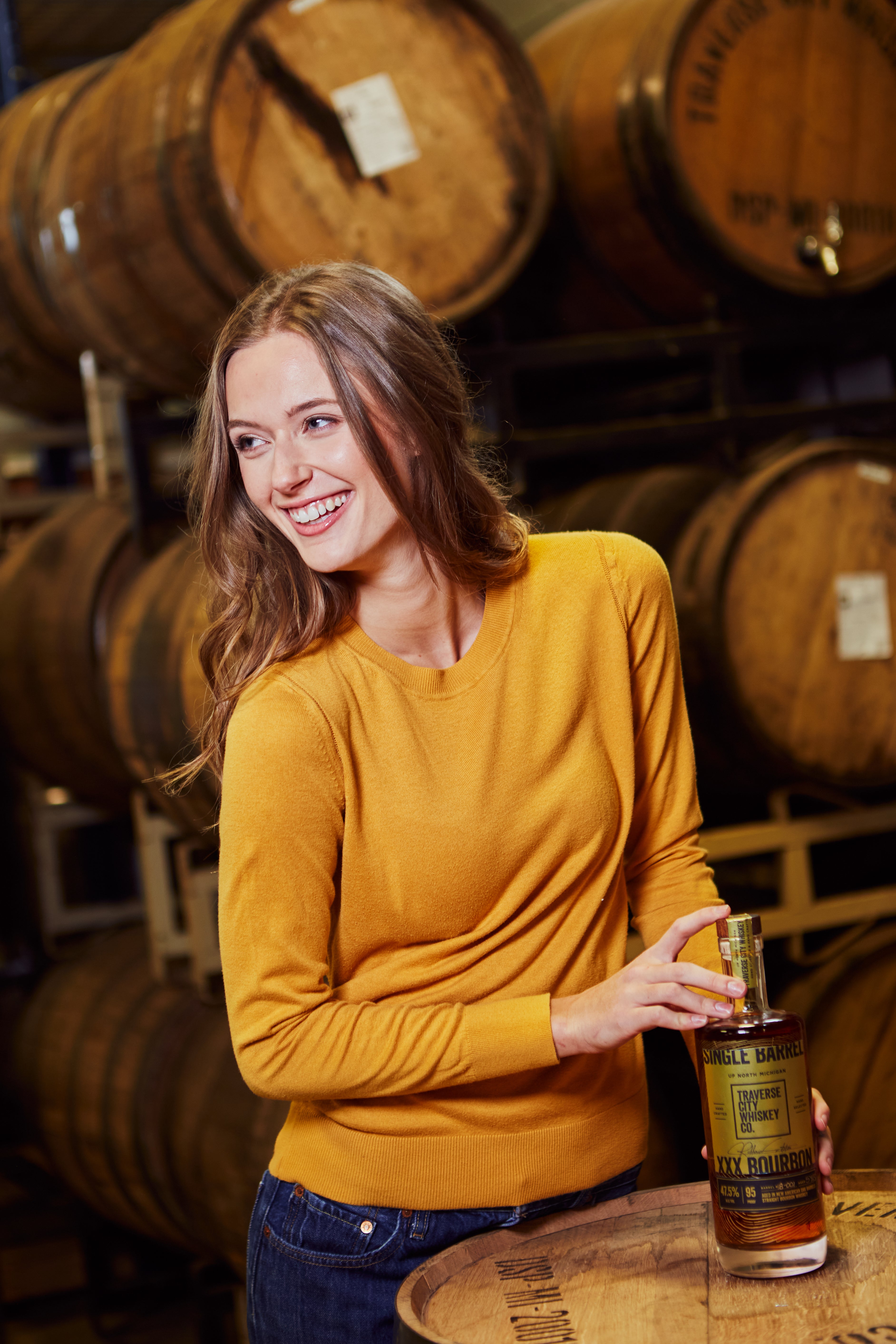 Woman in the rickhouse holding a bottle of Single Barrel XXX Straight Bourbon