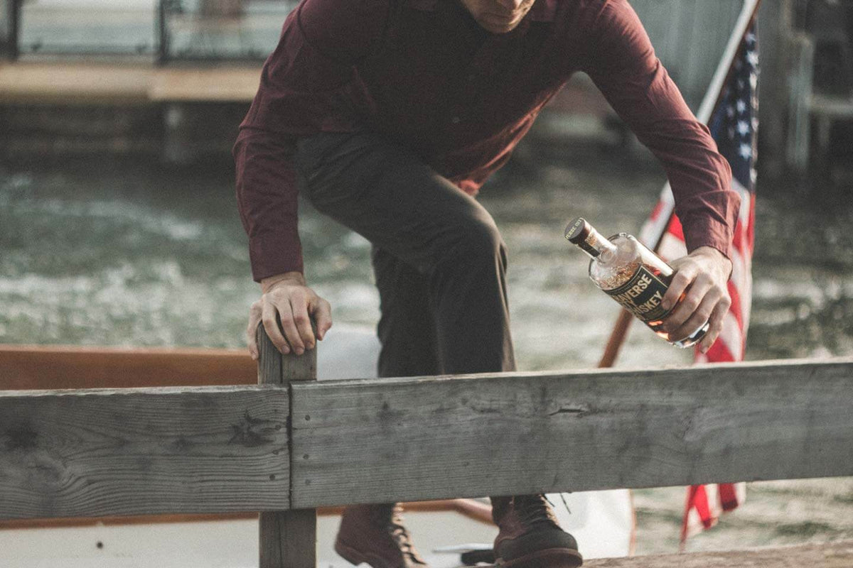Man sitting on a dock holding a bottle, with a blurred background