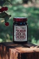 Premium Cocktail Cherries jar on a tree stump under a cherry branch