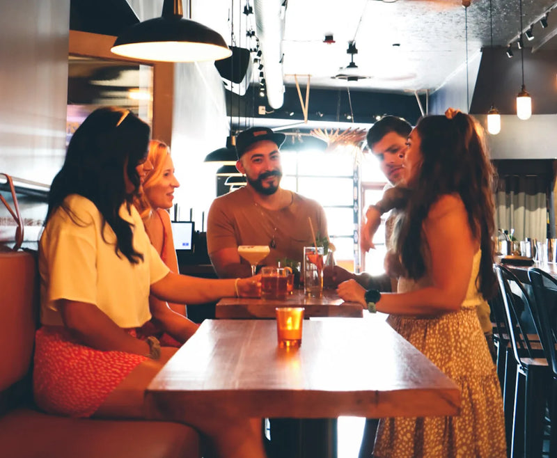 Friends gather around a table with cocktails at Traverse City Whiskey Co. Outpost in Ferndale